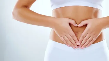 Mujer formando un corazón sobre su abdomen después de cirugía estética, cuidada por especialista en masajes postoperatorios en Barcelona.a
